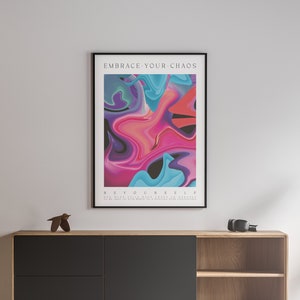 May include: A framed abstract art print with a colourful design of pink, blue, and purple swirls. The text "EMBRACE YOUR CHAOS" is at the top of the print and "BE YOURSELF" is at the bottom. The text below "BE YOURSELF" reads "ONE MUST STILL WALK CHAOS IN ONESELF TO BE ABLE TO GIVE BIRTH TO A DANCING STAR WITHIN."