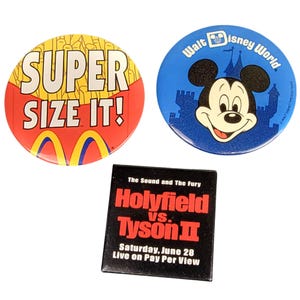 May include: Three round buttons with different designs. The first button is red with yellow and white accents and says "SUPER SIZE IT!" The second button is blue with white accents and features a cartoon Mickey Mouse. The third button is black with white text and says "The Sound and The Fury Holyfield vs. Tyson II Saturday, June 28 Live on Pay Per View".