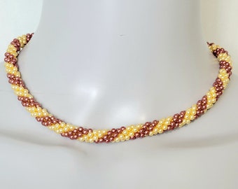 May include: A brown and cream beaded necklace with a twisted design. The necklace is made of small, round beads and is approximately 18 inches long.