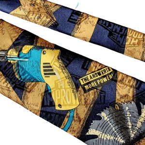 May include: A blue and gold tie with a power drill, saw, and wood pattern. The tie has the text "The Answers More Power!" printed on it.