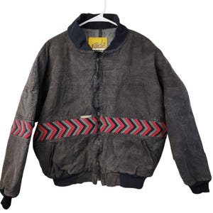 May include: A dark gray bomber jacket with a black collar and cuffs. The jacket features a red and gray geometric pattern across the chest. The brand name "rode" is visible on a yellow tag.