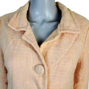May include: A pale peach tweed jacket with a single button closure. The jacket has a collar and long sleeves.