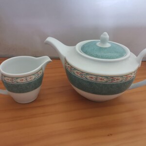 May include: A white teapot and creamer set with a green and gold geometric pattern. The teapot has a lid and a spout. The creamer has a handle.