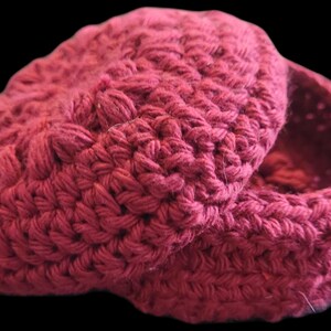 May include: A handmade, claret-coloured crochet box with a lid. The box and lid are made with a thick yarn, showcasing a textured stitch pattern. The lid is partially open, revealing the interior of the box.