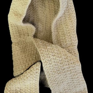 Peut inclure: Une écharpe à capuche de couleur crème en matière douce et duveteuse. L'écharpe est crocheté et a un design long et fluide.