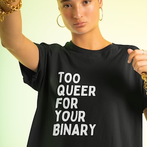 Może przedstawiać: Czarny t-shirt z białym napisem "TOO QUEER FOR YOUR BINARY". Koszulka ma okrągły dekolt i krótkie rękawy. Tło to gradient żółtego i zielonego.