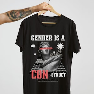 Könnte beinhalten: Schwarzes T-Shirt mit einem Grafikdruck einer klassischen Skulptur mit einem roten Strich über den Augen. Der Text "GENDER IS A CONSTRUCT" ist unter dem Bild gedruckt.
