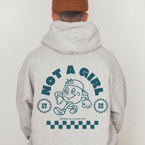 May include: A gray hoodie with a blue graphic on the back that says "Not a Girl" with a cartoon character and the text "Gender is a construct".