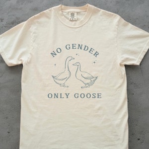 Puede incluir: Una camiseta beige con un gráfico de dos gansos y el texto "NO GENDER ONLY GOOSE".