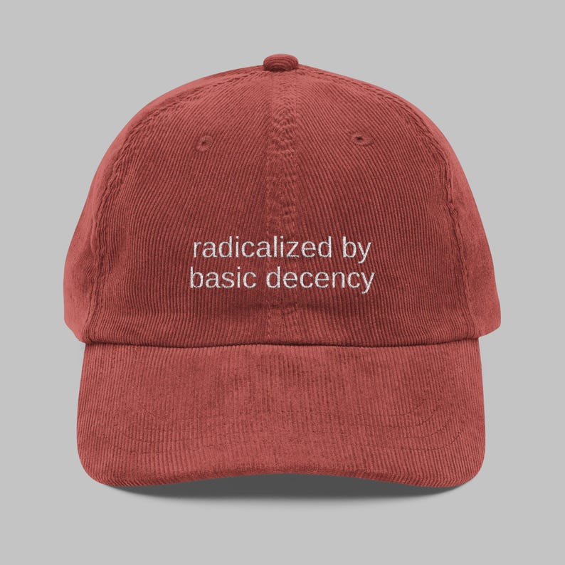 Puede incluir: Gorra de b&eacute;isbol de pana de color &oacute;xido con visera curva. La gorra presenta el texto bordado en blanco: "radicalized by basic decency". El gorro tiene una corona estructurada y una correa ajustable en la parte trasera.