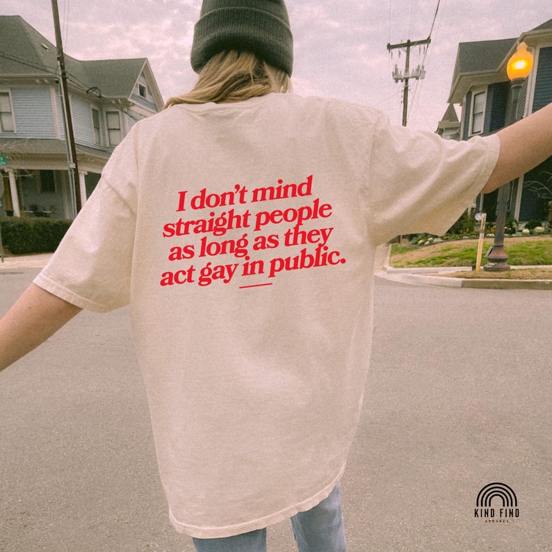 May include: Cream-colored t-shirt with the text "I don't mind straight people as long as they act gay in public" in red. The shirt is part of the Kind Find Apparel collection.