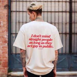 May include: Cream-colored t-shirt with the text "I don't mind straight people as long as they act gay in public" in red. The shirt is a casual style, with short sleeves and a relaxed fit. The brand logo is in the upper left corner.