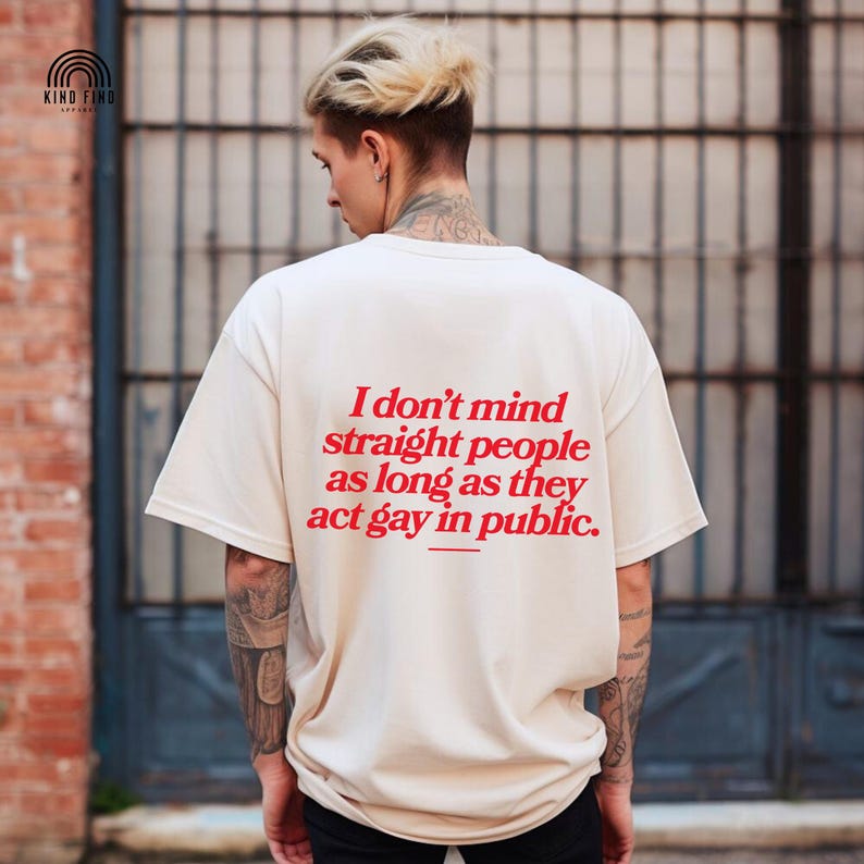 May include: Cream-colored t-shirt with the text "I don't mind straight people as long as they act gay in public" in red. The shirt is a casual style, with short sleeves and a relaxed fit. The brand logo is in the upper left corner.