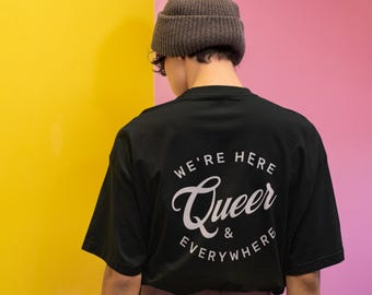 Puede incluir: Camiseta negra con un gráfico circular blanco en la espalda que dice "We're Here Queer & Everywhere".