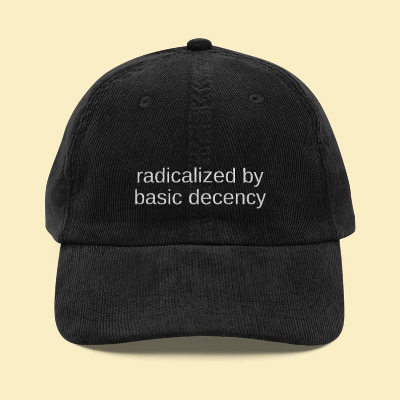 Puede incluir: Gorra de b&eacute;isbol de pana negra con la frase blanca "radicalized by basic decency". La gorra tiene una visera curva y un bot&oacute;n en la parte superior.