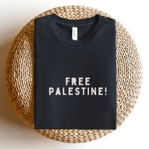 K&ouml;nnte beinhalten: Schwarzes T-Shirt mit dem Aufdruck "FREE PALESTINE!" in Wei&szlig; auf der Vorderseite.