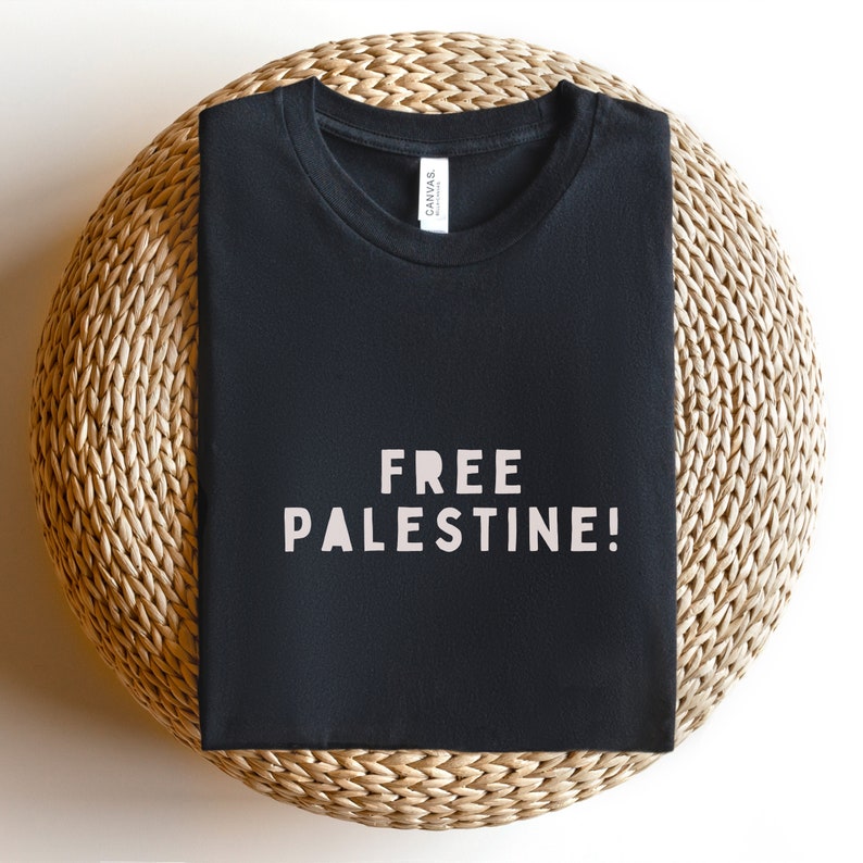 K&ouml;nnte beinhalten: Schwarzes T-Shirt mit dem Aufdruck "FREE PALESTINE!" in Wei&szlig; auf der Vorderseite.