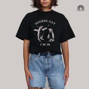 May include: Black t-shirt with a graphic of two penguins dancing and the text "SOUNDS GAY I'M IN"