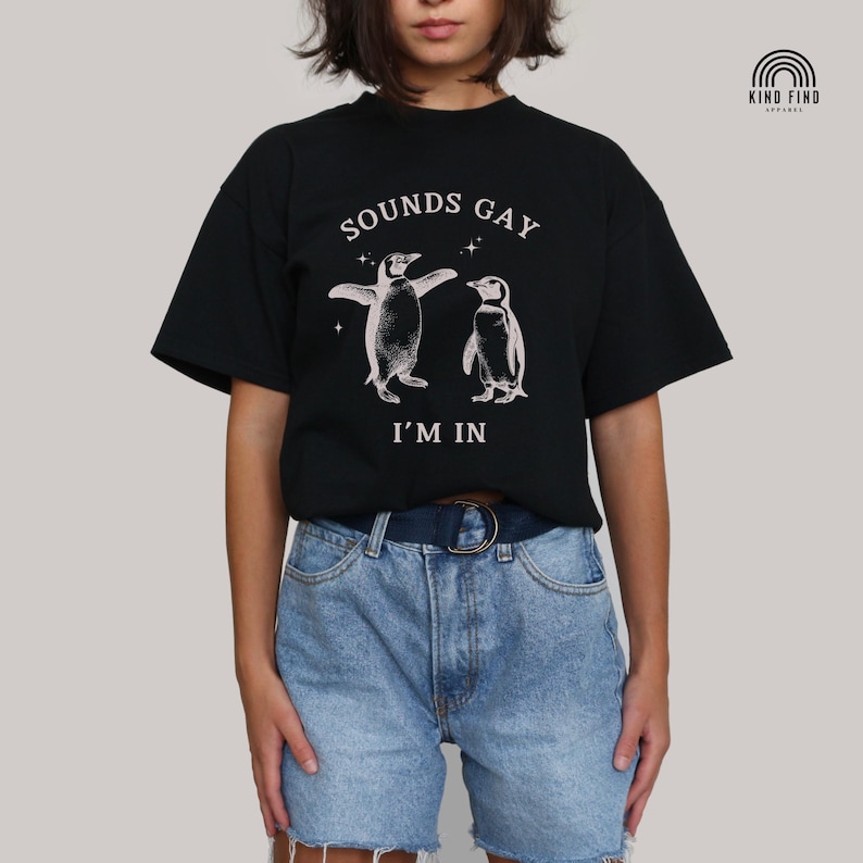 May include: Black t-shirt with a graphic of two penguins dancing and the text "SOUNDS GAY I'M IN"