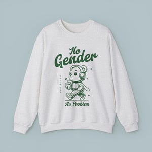 Op de afbeelding: Een lichtgrijs sweatshirt met een groene afbeelding van een cartoonbeer met een koptelefoon en een drankje. De tekst "No Gender" staat boven de beer en "Just Be You" en "No Problem" staan onder de beer.