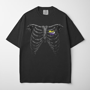 May include: Black t-shirt featuring a detailed illustration of a rib cage with a heart-shaped design in the center. The heart design incorporates yellow, white, and purple colors. The shirt has a crew neck and short sleeves.