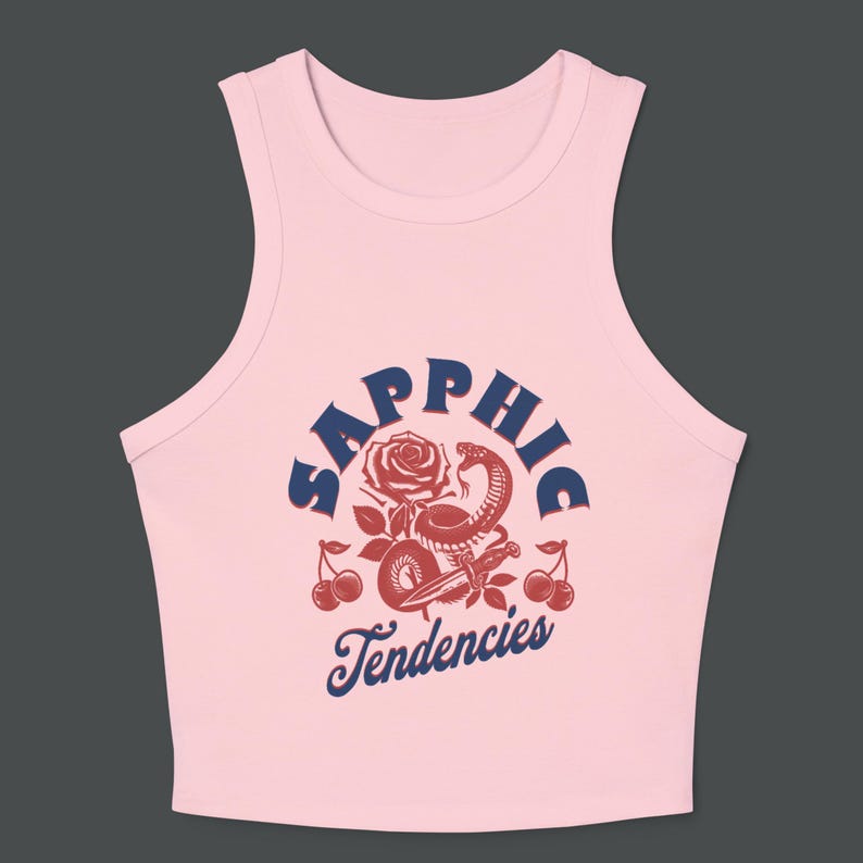 Puede incluir: Top corto rosa claro con un dise&ntilde;o gr&aacute;fico. El dise&ntilde;o presenta la palabra "Sapphic" en texto azul marino arqueado sobre una rosa roja, una serpiente y cerezas. Las palabras "Tendencies" est&aacute;n debajo.