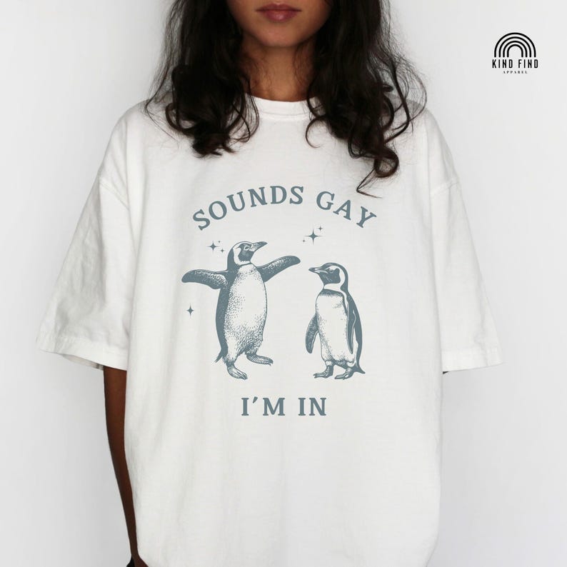 May include: White t-shirt with a graphic of two penguins and the text "Sounds Gay I'm In"