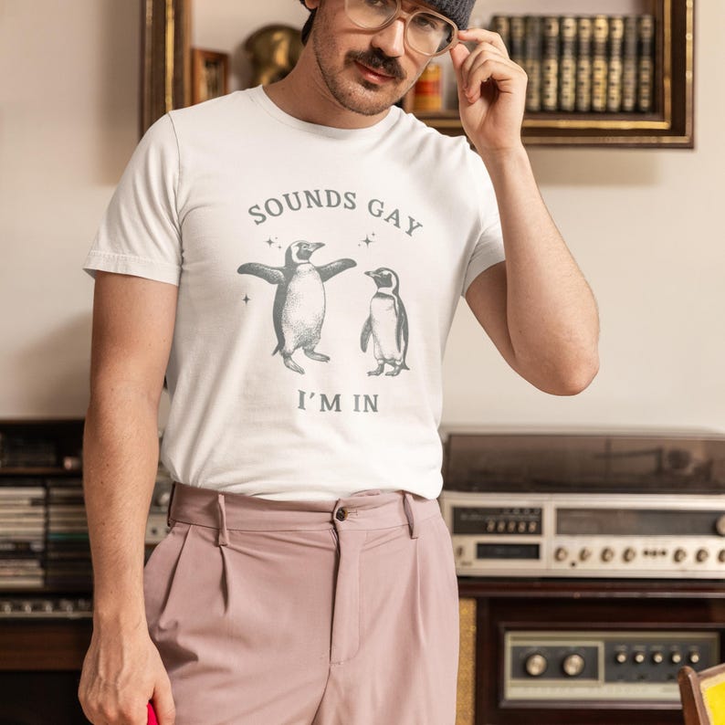 May include: White t-shirt with a graphic of two penguins dancing and the text "Sounds Gay I'm In."