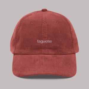 Könnte beinhalten: Rostfarbene Cord-Baseballkappe mit dem Wort "faguette" in Weiß gestickt. Die Kappe hat einen gebogenen Schirm und eine runde Krone. Ein klassischer Hut.