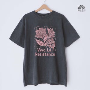 May include: Dark gray t-shirt with a pink floral design and the text "Vive La Resistance." The shirt has short sleeves and a crew neck. The brand logo is in the upper right corner.