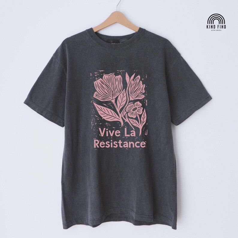 May include: Dark gray t-shirt with a pink floral design and the text "Vive La Resistance." The shirt has short sleeves and a crew neck. The brand logo is in the upper right corner.