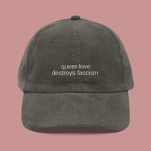 Può includere: Cappellino da baseball in velluto a coste verde oliva con la scritta bianca "queer love destroys fascism" ricamata. Il cappellino ha una visiera curva e un cinturino regolabile sul retro.