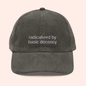 Puede incluir: Gorra de b&eacute;isbol de pana verde oscuro con la frase "radicalized by basic decency" bordada en blanco. La gorra tiene una visera curva y una correa ajustable.