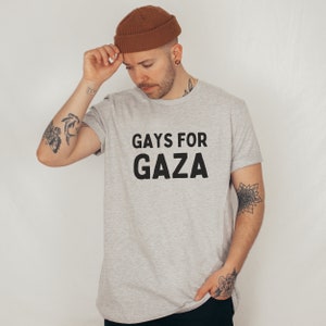 May include: A gray t-shirt with the text "GAYS FOR GAZA" printed in black. The person wearing the shirt is wearing a brown beanie.