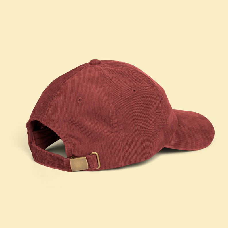 Puede incluir: Gorra de b&eacute;isbol de pana burdeos con visera curva. La gorra tiene un cierre de hebilla ajustable de color lat&oacute;n en la parte trasera. La gorra est&aacute; hecha de tela acanalada.