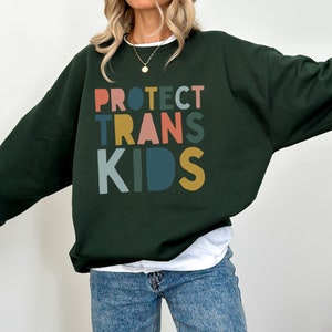 May include: A dark green sweatshirt with the words "PROTECT TRANS KIDS" printed in colourful letters.