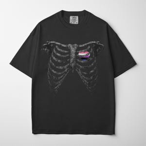 May include: Black t-shirt featuring a detailed illustration of a rib cage with a heart-shaped design in the center. The heart design incorporates pink, purple, and blue colors. The shirt has a crew neck and short sleeves.