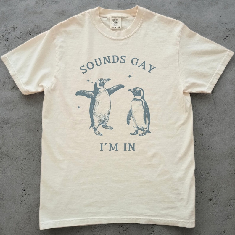 sounds gay i'm in with 2 vintage illustrations of penguins in blue on an ivory comfort colors tshirt