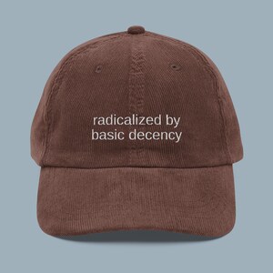 Puede incluir: Gorra de b&eacute;isbol de pana marr&oacute;n con la frase "radicalized by basic decency" bordada en blanco. La gorra tiene una visera curva y un bot&oacute;n en la parte superior. Un accesorio casual.