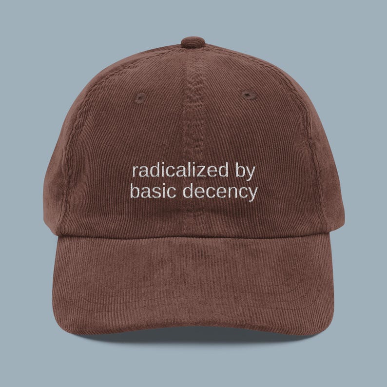 Puede incluir: Gorra de b&eacute;isbol de pana marr&oacute;n con la frase "radicalized by basic decency" bordada en blanco. La gorra tiene una visera curva y un bot&oacute;n en la parte superior. Un accesorio casual.