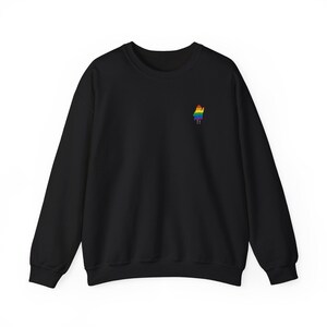 May include: Black crew neck sweatshirt featuring a small, embroidered rainbow figure on the left chest. The figure is a person-shaped design with a rainbow-coloured outfit. The sweatshirt has long sleeves and a classic, casual style.