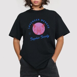May include: Black t-shirt with a pink circle graphic featuring two mermaids and the text "Lavender Menace Sapphic Society EstD 1970"