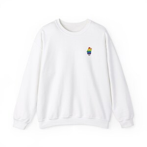 May include: White crew neck sweatshirt featuring a small, embroidered figure on the left chest. The figure is a person with a rainbow-coloured outfit. The sweatshirt has long sleeves and a classic, casual design.
