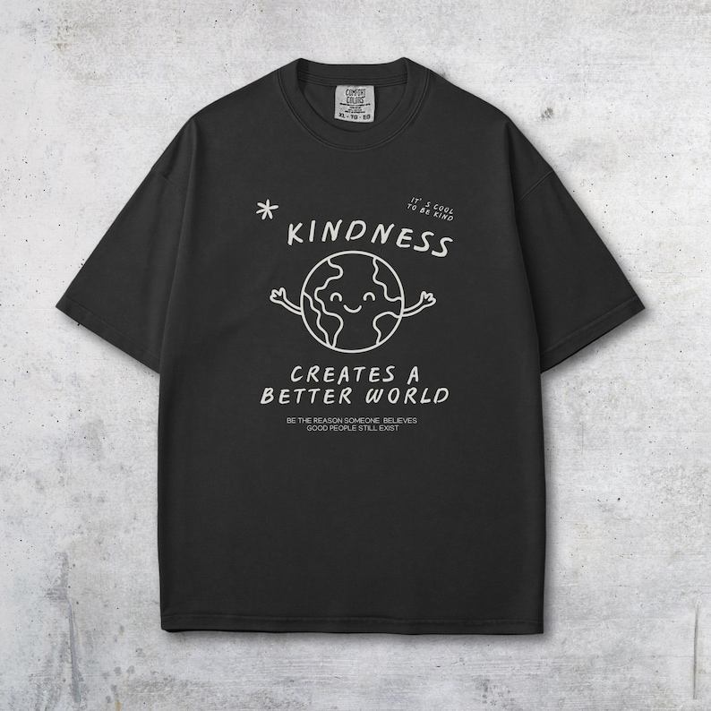 May include: Black t-shirt featuring a white graphic of a smiling globe with arms, the word "KINDNESS", and the phrase "CREATES A BETTER WORLD". The shirt also includes the text "BE THE REASON SOMEONE BELIEVES GOOD PEOPLE STILL EXIST".