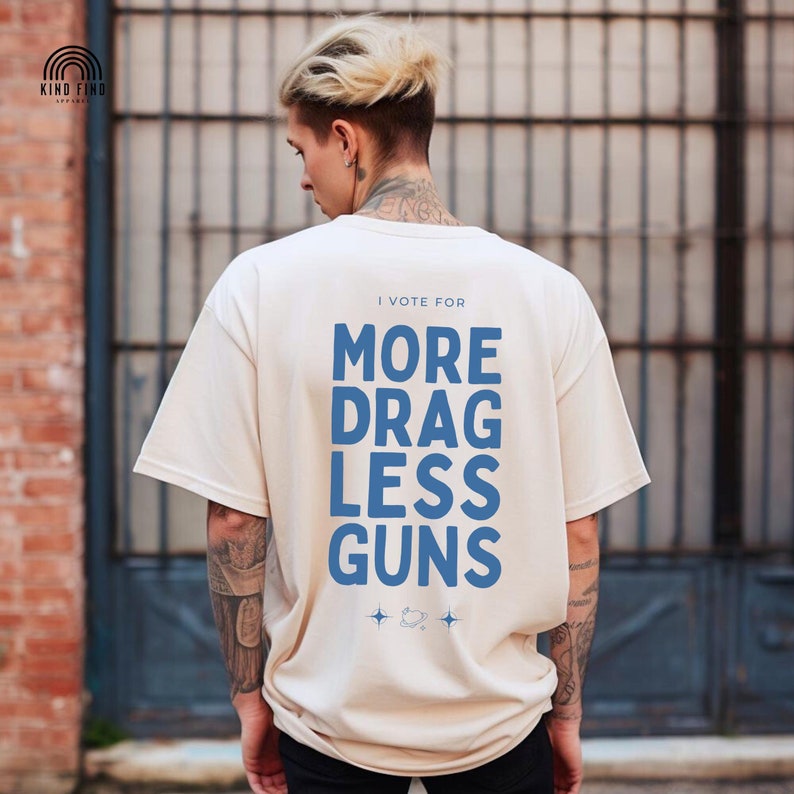 the words 'I vote for more drag less guns' in a stylish typography design on the back of an ivory comfort colors shirt