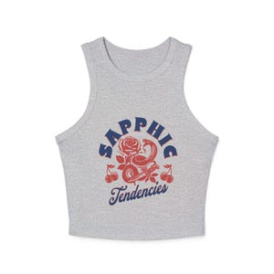 Puede incluir: Una camiseta sin mangas gris con un dise&ntilde;o gr&aacute;fico. El dise&ntilde;o presenta la palabra "Sapphic" en azul, una rosa roja, una serpiente roja y cerezas. Las palabras "Tendencies" est&aacute;n escritas en azul debajo.