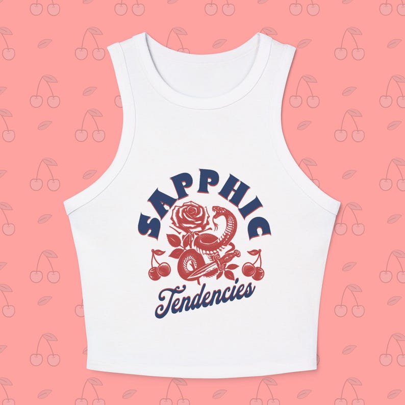 Puede incluir: Top corto blanco con un dise&ntilde;o gr&aacute;fico que presenta una rosa roja, una serpiente y cerezas, con el texto "Sapphic Tendencies" en azul marino. El top es sin mangas y tiene cuello redondo.