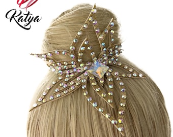 May include: A gold-toned hair accessory in a starburst design, adorned with iridescent rhinestones and a central, square-cut crystal. The accessory is attached to blonde hair. The brand name "Katya" is displayed in the upper left corner.