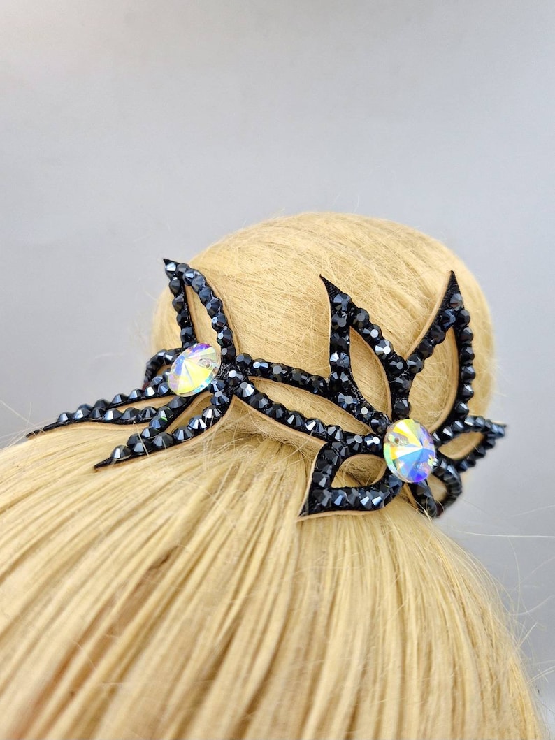 May include: Black hair accessory with crystal embellishments in the shape of two stylised leaves.