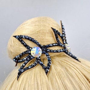 May include: A black hair clip with a large, clear rhinestone in the centre. The clip is shaped like a flower with multiple petals.